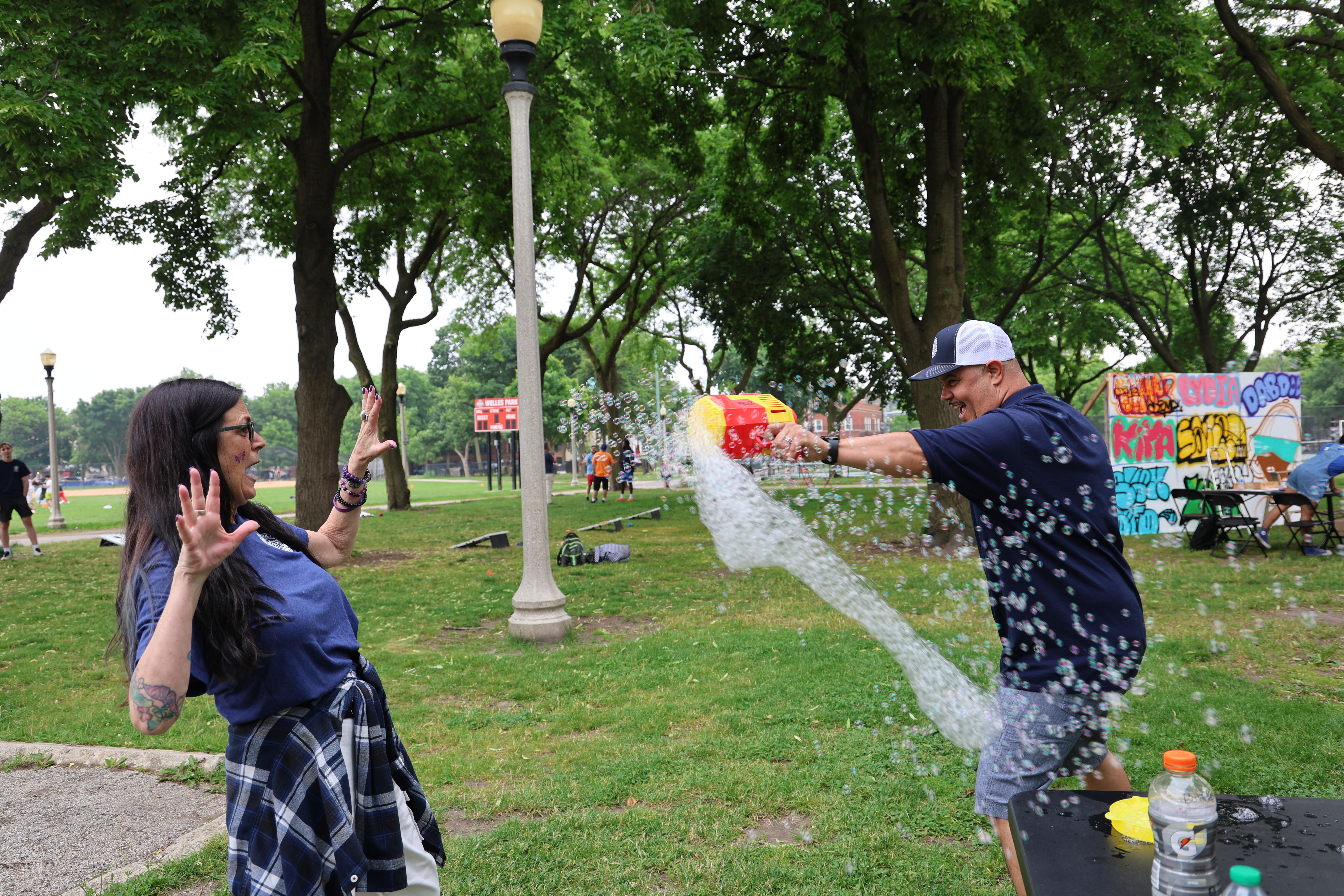 Man aims a bubble gun at a woman in a park.